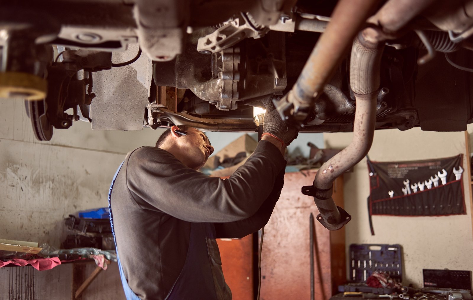 Side cropped view of auto repairman bending under bottom of car while fixing exhaust system of car.