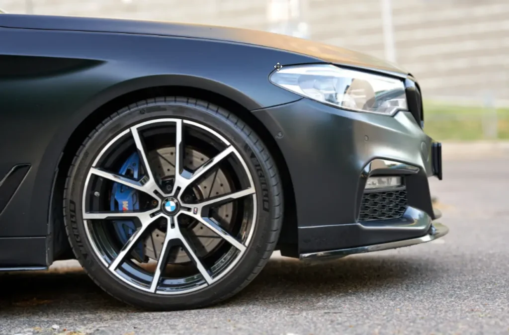 BMW Service & Repair In Tomball, TX At Jon's Auto & Diesel Repair. Image Front wheel, tire, and blue brake caliper of a matte black BMW.