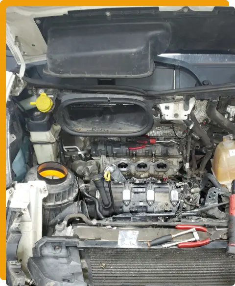 Engine Repair In Tomball TX At Jon’s Auto & Diesel Repair. A car engine with the valve cover removed, showing exposed spark plug wells and engine components. Various tools and engine parts are visible around the engine bay.