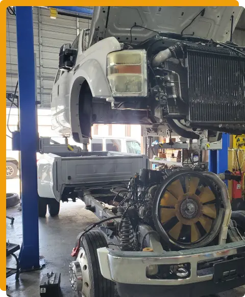 Fleet Services In Tomball TX At Jon’s Auto & Diesel Repair. A large truck in a repair shop is lifted, with its cab raised and engine exposed. Tools and equipment are visible in the background.