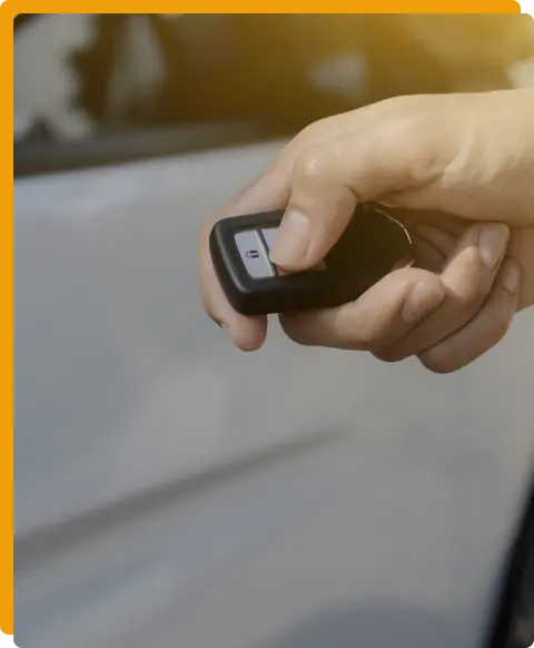 Key Fob Programming Services In Tomball TX At Jon’s Auto & Diesel Repair. A hand holding a car key fob, pressing a button near a white car door, with sunlight in the background.