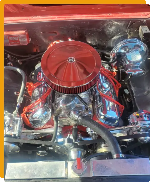 Performance Upgrades & Kits In Tomball TX At Jon’s Auto & Diesel Repair. A close-up view of a shiny, modified car engine with red and chrome components, red ignition wires, and various metal parts inside an engine bay.