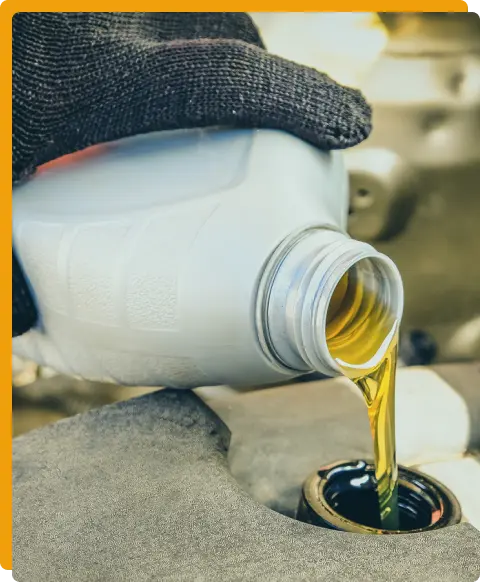 Preventative Maintenance In Tomball TX At Jon’s Auto & Diesel Repair. A gloved hand pours golden engine oil from a plastic bottle into a vehicle’s oil reservoir, with the engine components visible in the background.