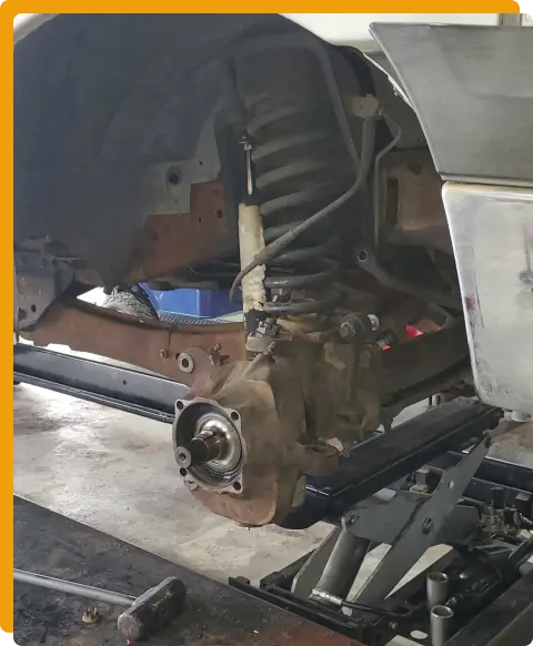 Suspension Repair In Tomball TX At Jon’s Auto & Diesel Repair. A close-up view of a vehicle’s front suspension and wheel hub assembly, with the wheel removed and tools nearby, inside a garage or workshop setting.