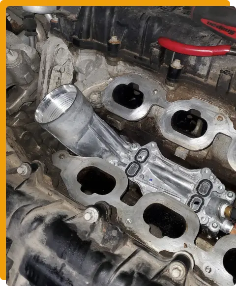 Duramax Engine Repair In Tomball TX At Jon’s Auto & Diesel Repair. A close-up of a car engine intake manifold with an aluminum replacement part installed, surrounded by engine components and tools.