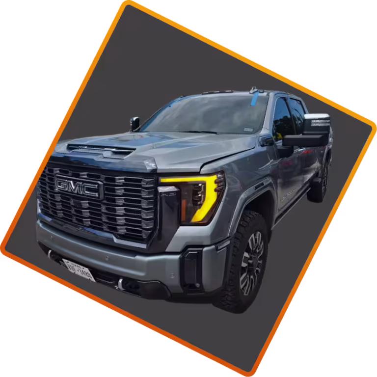 A silver GMC pickup truck is shown at an angle against a dark, tilted background with an orange border. The truck has large tires, prominent grille, and modern headlights.